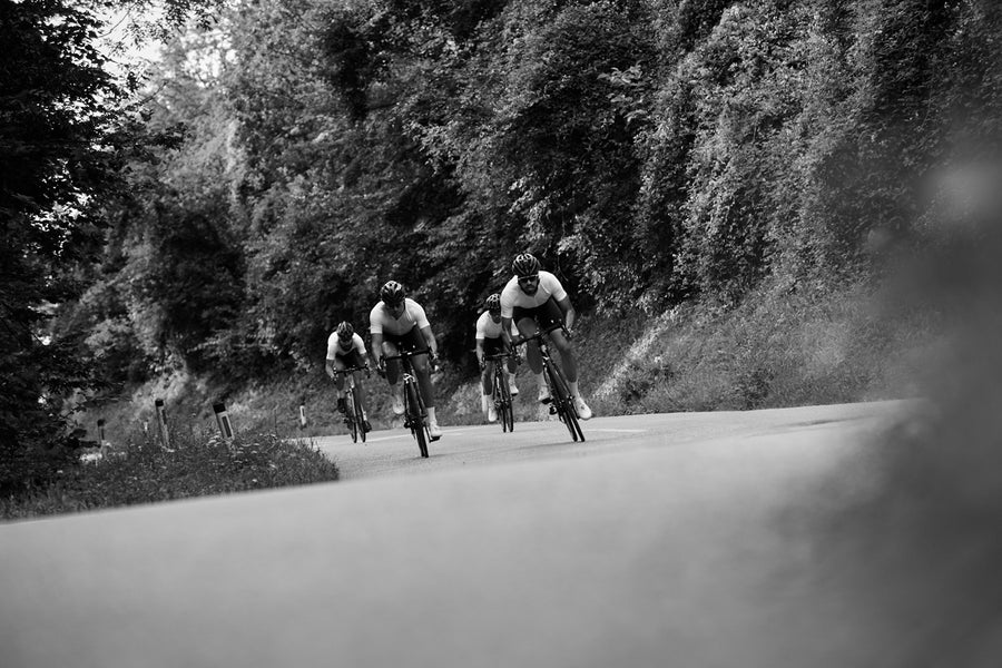 A club bunch riding together on a wooded climb in custom kit